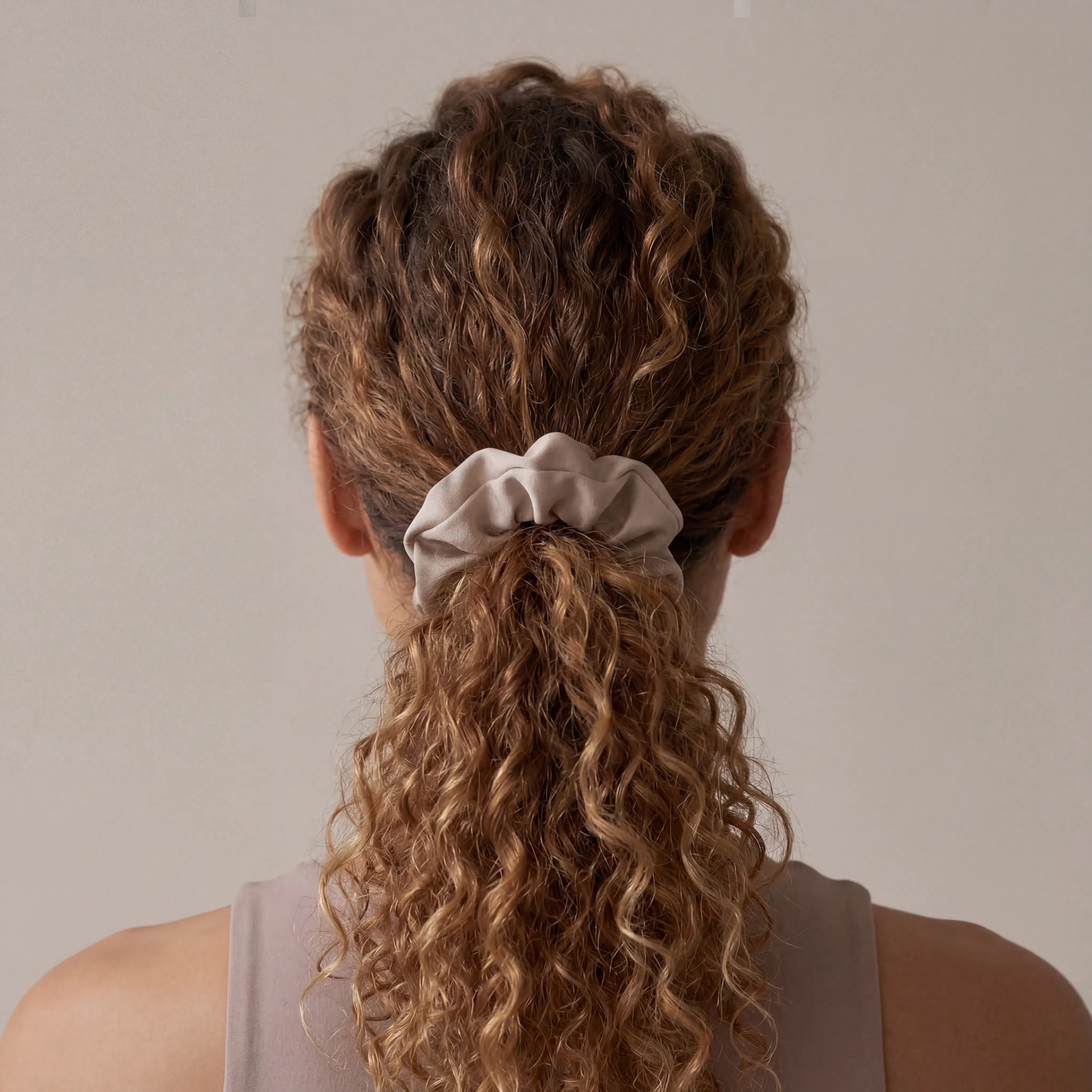 Person with curly hair tied back with a scrunchie against a neutral background