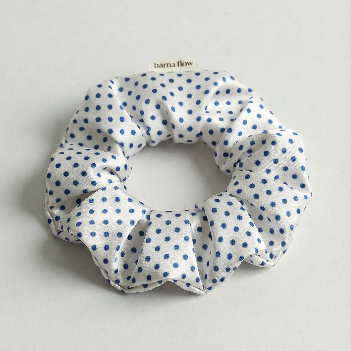 White scrunchie with blue polka dots on a light gray background