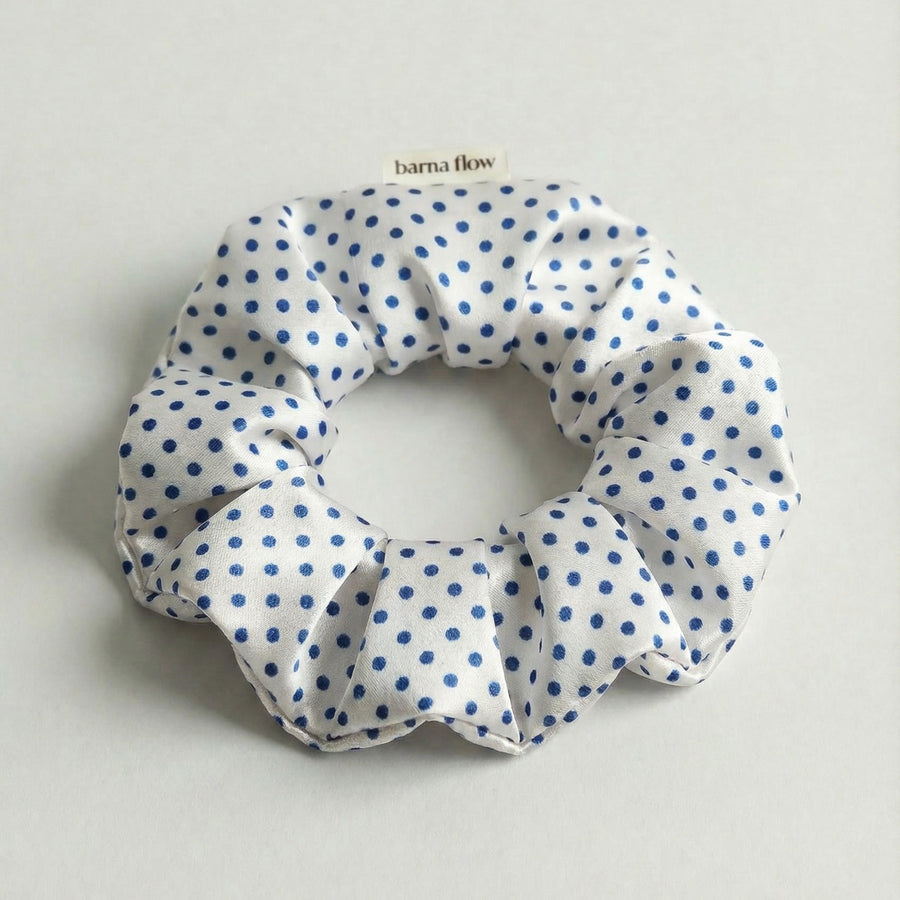 White scrunchie with blue polka dots on a light gray background