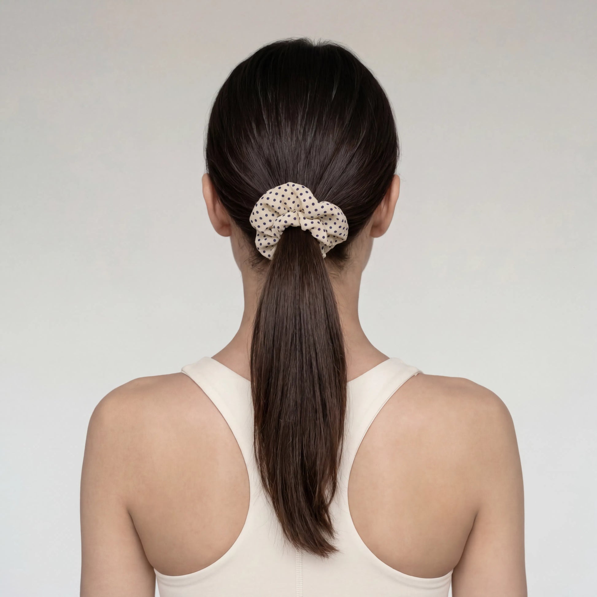 Woman with a ponytail wearing a polka dot scrunchie close up against a plain background