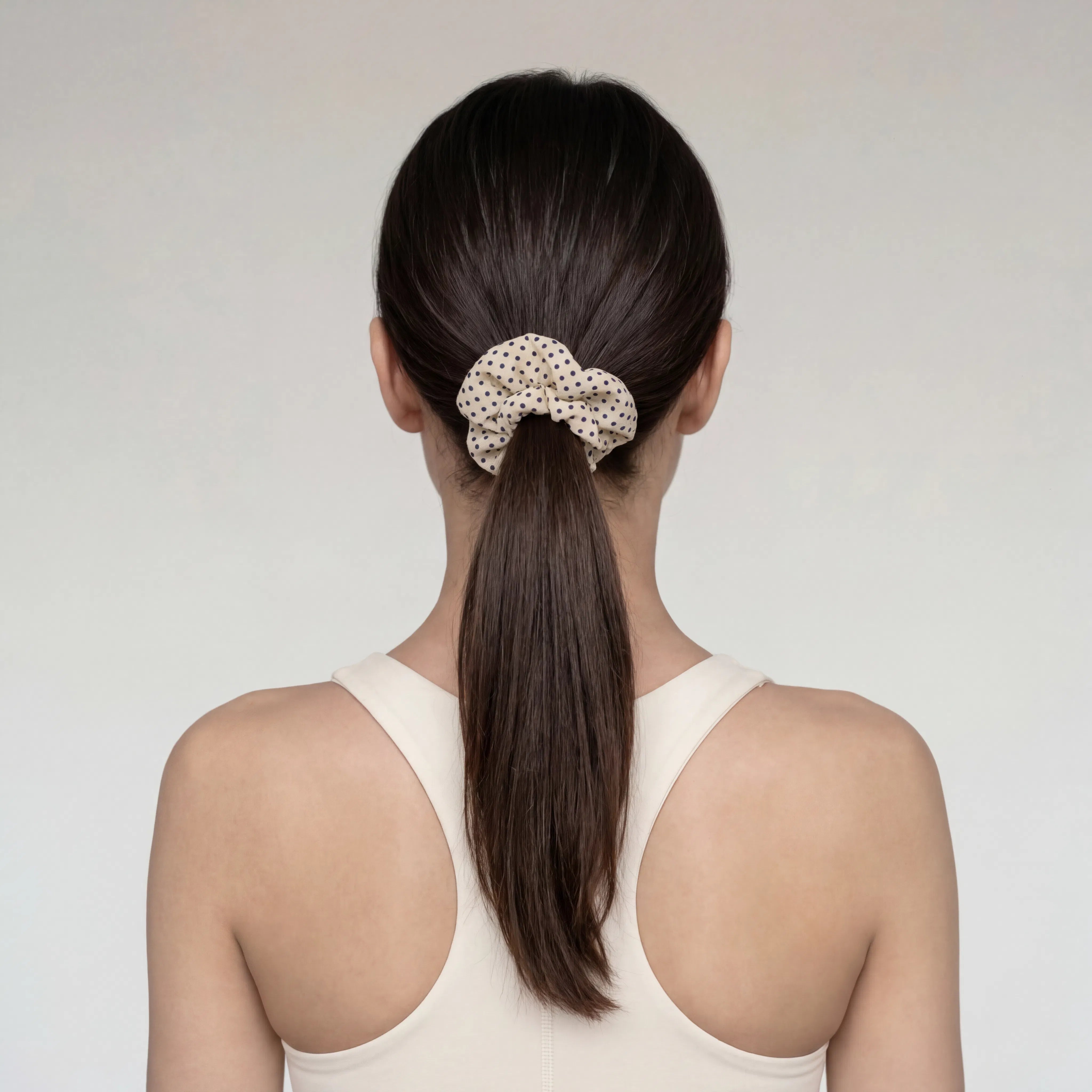 Woman with a ponytail wearing a polka dot scrunchie close up against a plain background