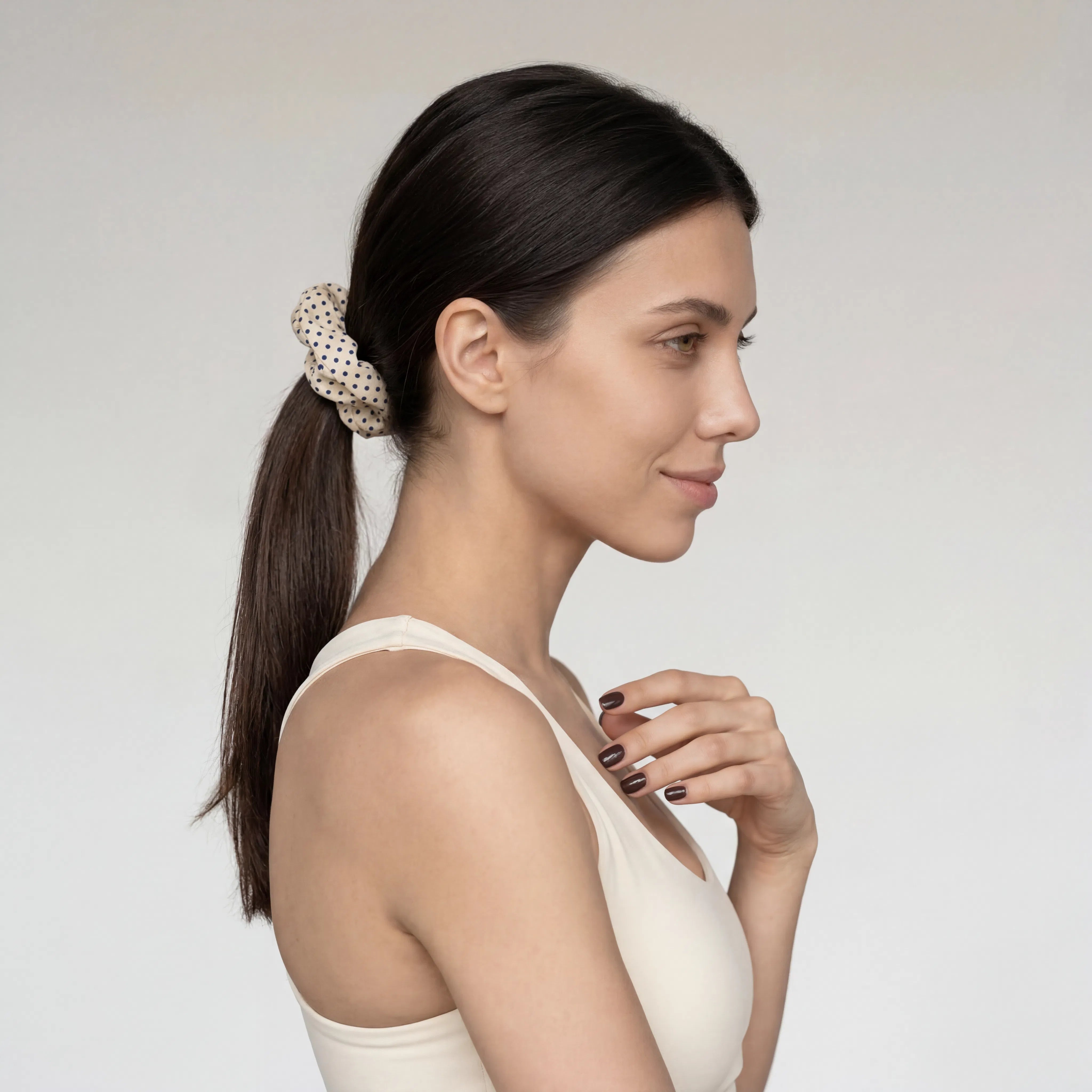 Woman with a ponytail wearing a polka dot scrunchie against a plain background